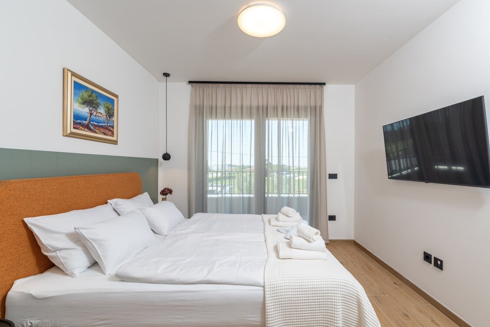 Hotellihuone, jossa on sänky, taulu, televisio ja ikkuna, jossa on verhot.