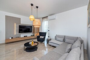 Ein modernes Wohnzimmer mit großem Flachbildfernseher, einem grauen Sofa, einem schwarzen Sessel und einem runden Couchtisch.