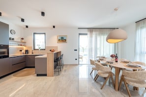 A modern kitchen with a central island, dining area with wicker chairs, and a large pendant light.