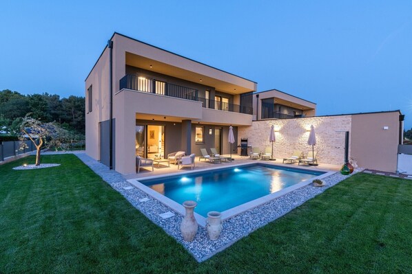 A modern two-story house with a swimming pool, outdoor seating, and a stone wall.
