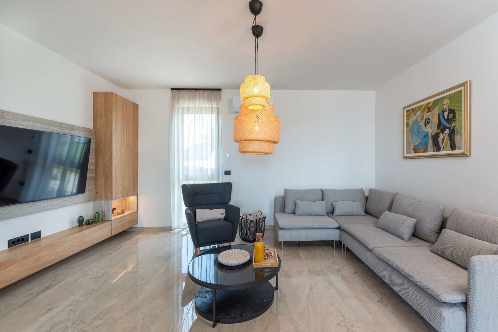 En moderne stue med et fladskærms-tv, en sofa, en lænestol, et sofabord og en hængende lampe.