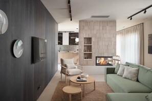 Ein modernes Wohnzimmer mit Kamin, einem wandmontierten Flachbildfernseher, einem grünen Sofa und einem Holztisch.