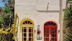 Ein Gebäude mit zwei Rundbogen-Türen, eine gelb und eine rot, und einem großen weißen Blumenkübel in der Mitte.