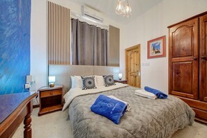 Ein Schlafzimmer mit Bett, Nachttischen, einem Kleiderschrank, einem Gemälde und einem Fenster mit Jalousien.