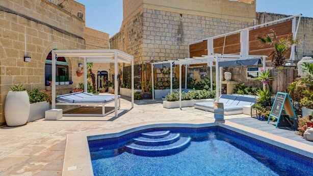 Ein Poolbereich mit bepflastertem Pool, Liegestühlen und einer Pergola.