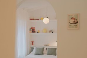 A bedroom with a bed, pillows, a shelf with books and decorative items, a lamp, and a poster on the wall. - Cute studio in a tiny house right next to the lake (Sala Comacina)