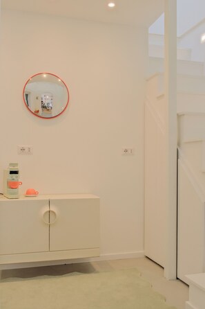 A minimalist room with a white dresser, a round mirror with a red frame, a small coffee machine, and a light green rug. - Cute studio in a tiny house right next to the lake (Sala Comacina)