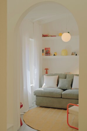 A room with a sofa, a round woven rug, a red chair, and a bookshelf with books and decorative items. - Cute studio in a tiny house right next to the lake (Sala Comacina)