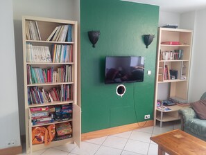 Una sala de estar con una estantería, un televisor instalado en la pared y una pared de acento verde.