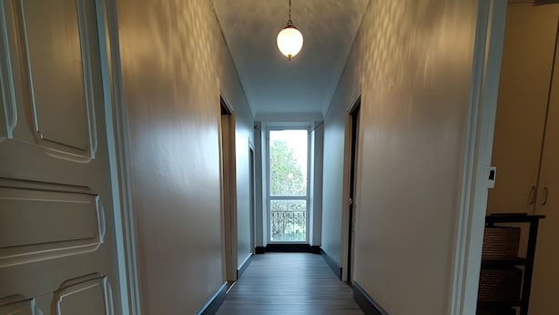 A hallway with wooden flooring, white walls, and a ceiling light.