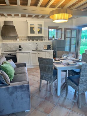 A modern kitchen with white cabinets, a built-in oven, and a dining area with wicker chairs and a table set for two. - View of Castelvecchio exclusive Tuscan guest house in the countryside of Lucca (Castelvecchio di Cómpito)