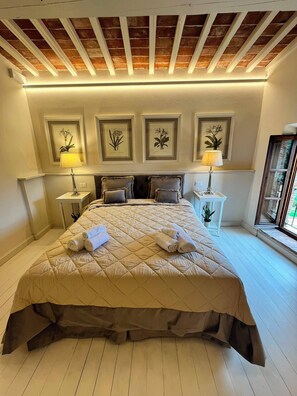Une chambre à coucher avec un grand lit, une tête de lit, des tables de chevet avec des lampes, des reproductions botaniques encadrées et un plafond en bois.