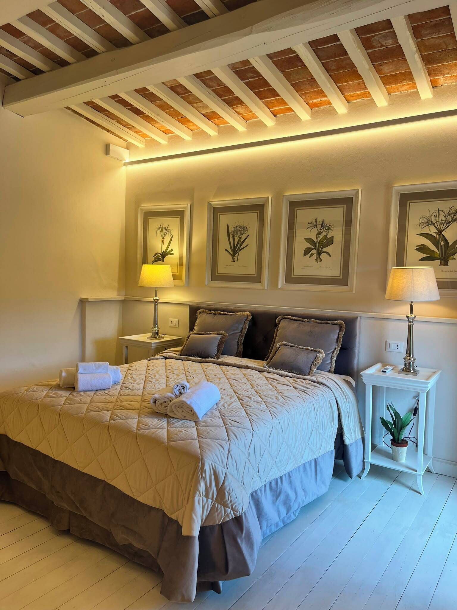 A bedroom with a bed, bedside tables, lamps, and framed botanical prints on the wall.