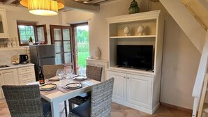 Zona pranzo con tavolo apparecchiato per quattro, circondata da sedie in vimini, un mobile bianco con oggetti decorativi e un televisore su uno scaffale.