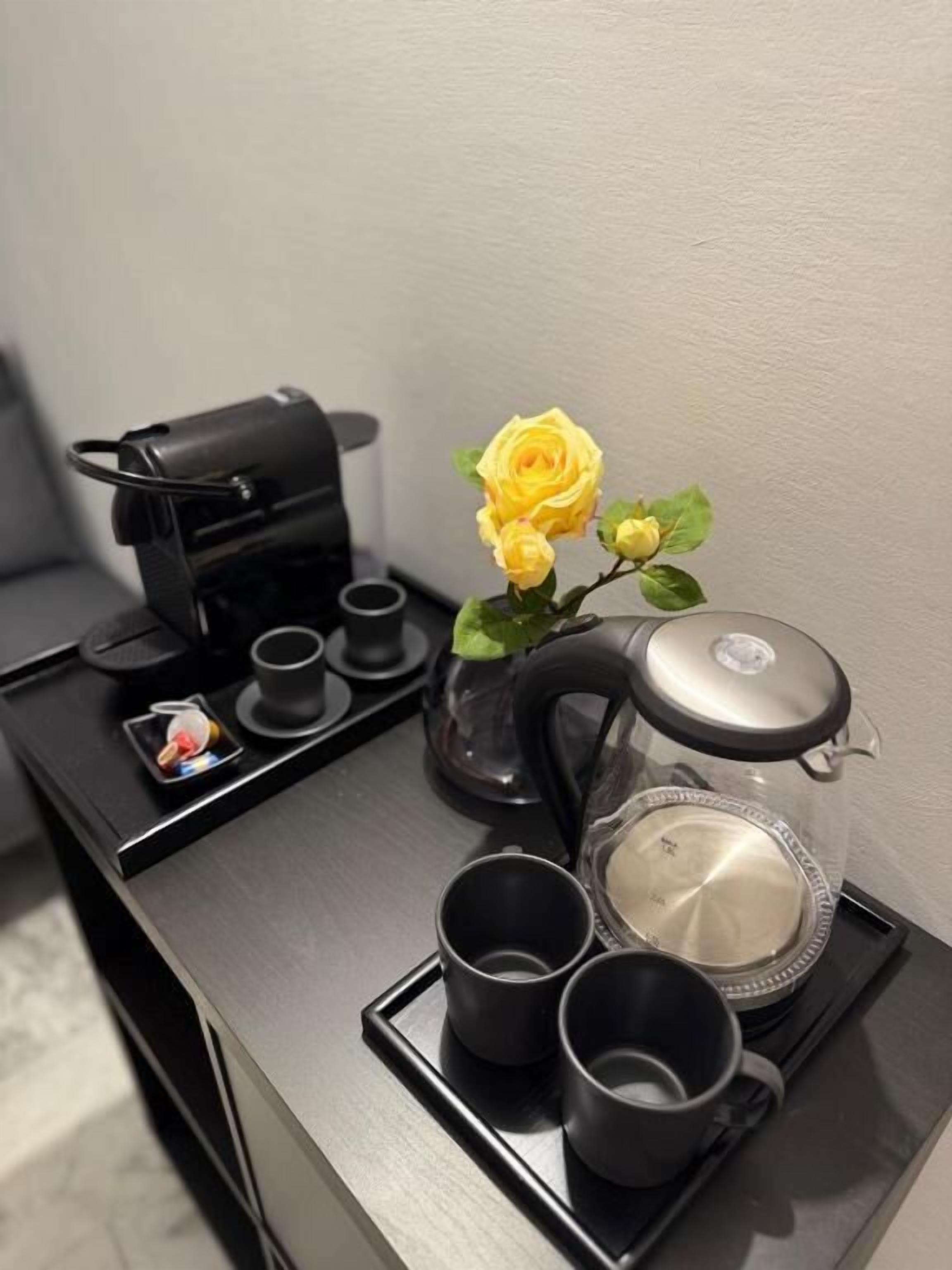 A kitchen area with a coffee maker, a tea kettle, a teapot, and a tray with cups.