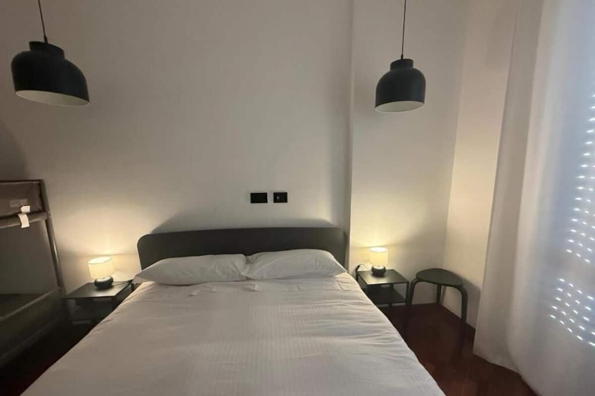 Habitació d'hotel amb un llit gran, dues làmpades de nit, una cadira i dues làmpades fixades a la paret.