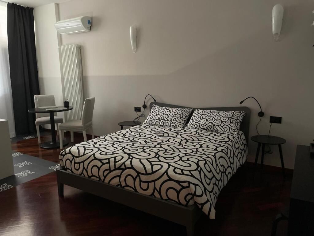 A hotel room with a bed, a chair, a small table, and a radiator.