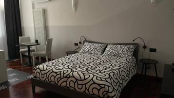A hotel room with a bed, a chair, a small table, and a radiator.