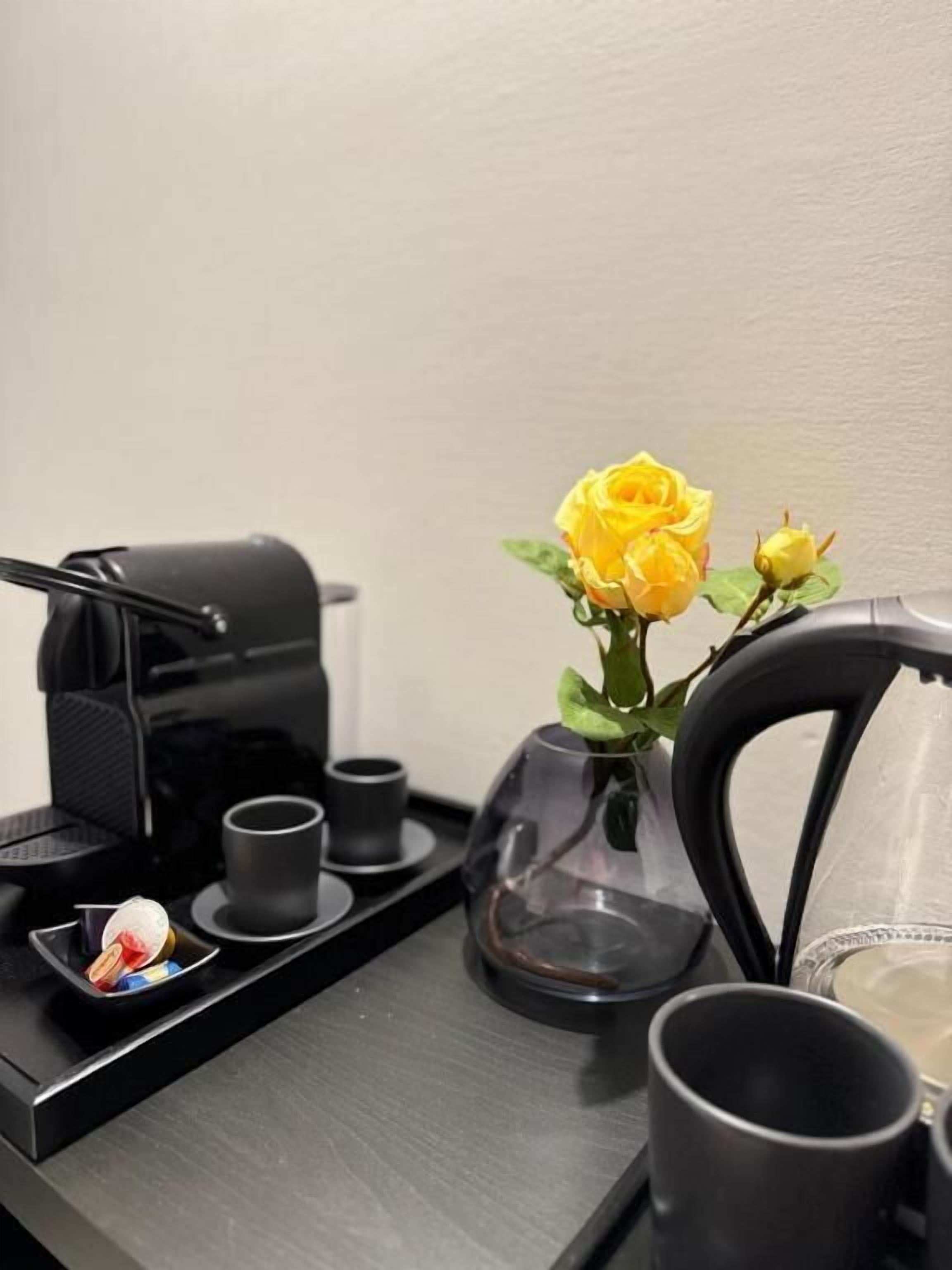 Une machine à café, un vase avec des fleurs jaunes et un plateau avec des tasses et une petite assiette.