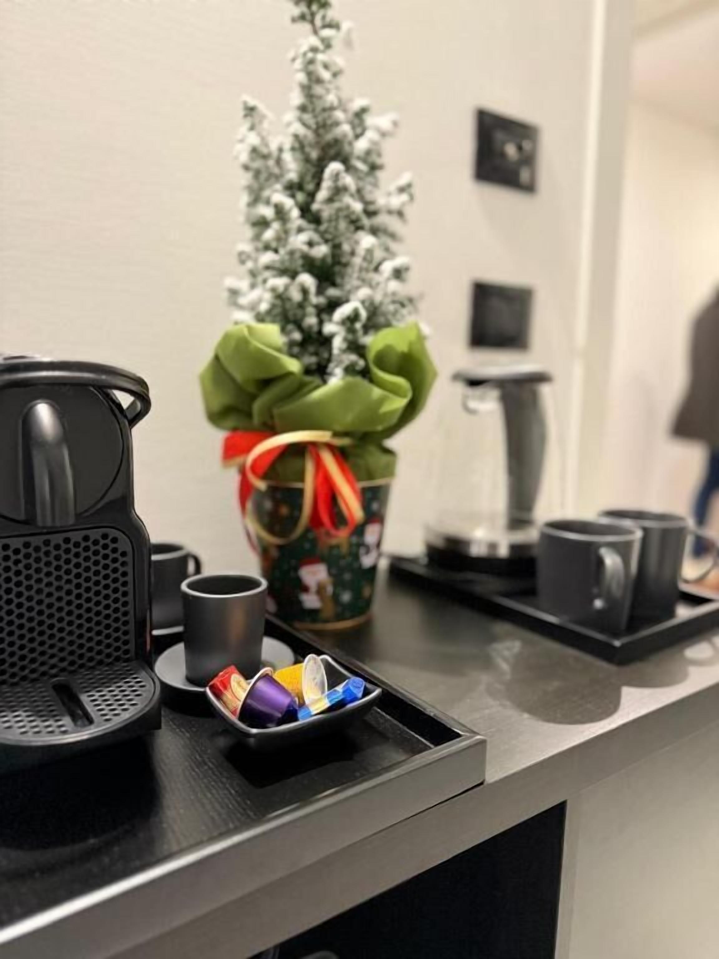 En kaffebryggare, en mugg, ett litet bricka med färgglada koppar och en julgran med ett grönt band.