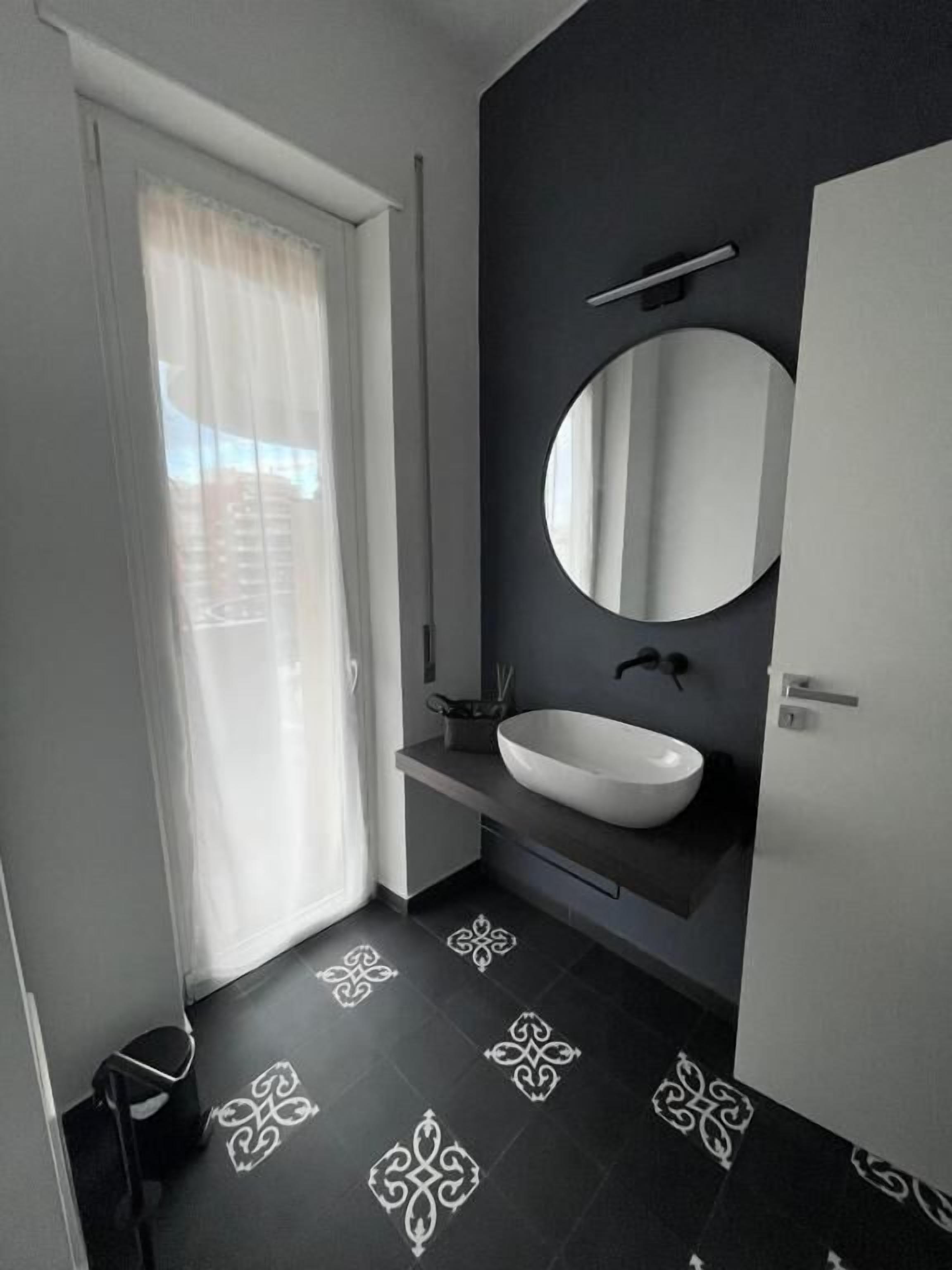 Un baño moderno con un lavabo blanco, un espejo grande y un piso con diseño.