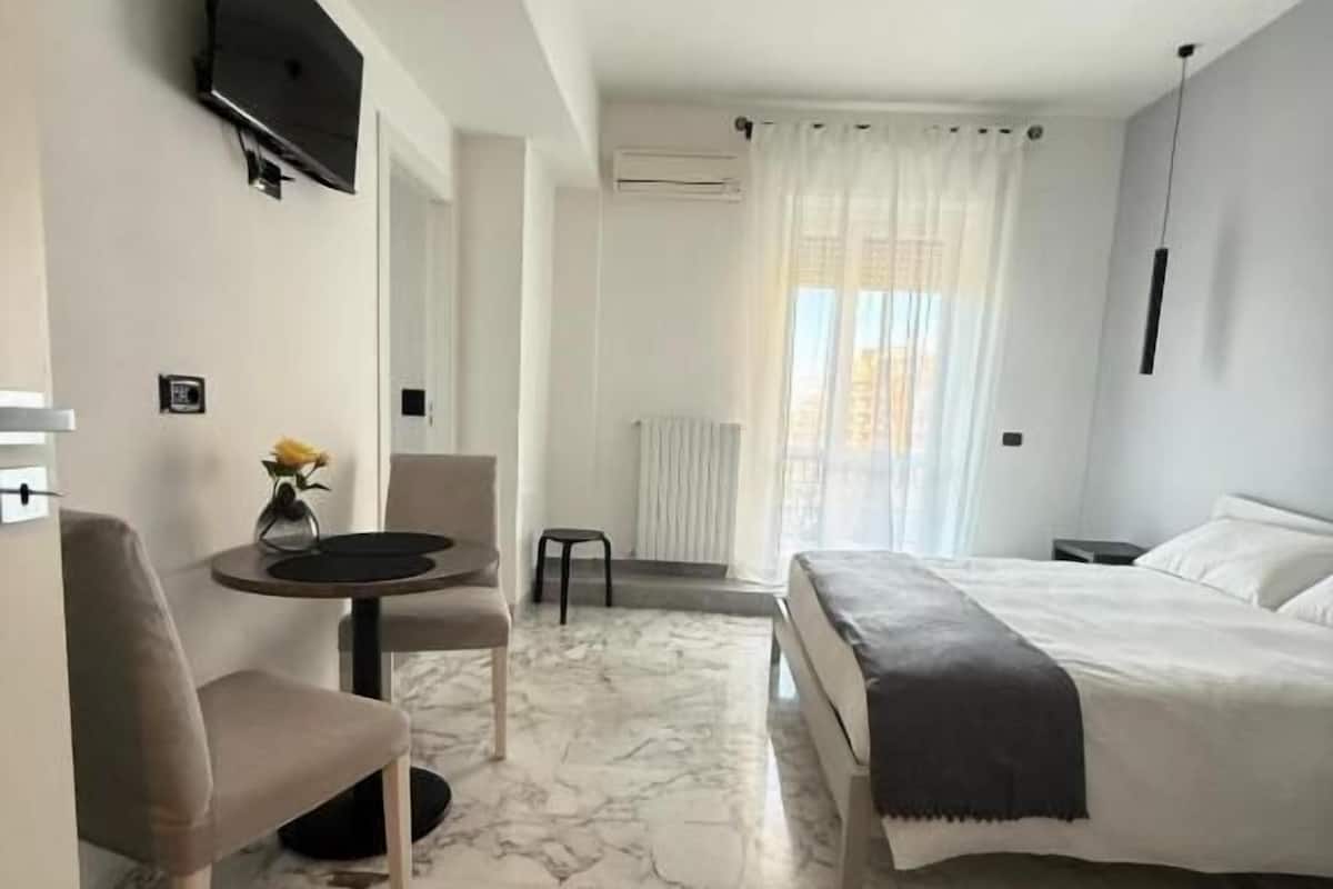 Una habitació d'hotel amb llit, escriptori, cadira, televisió i finestra amb cortines.