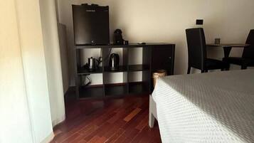 A hotel room with a bed, a desk, a chair, a television, and a minibar.