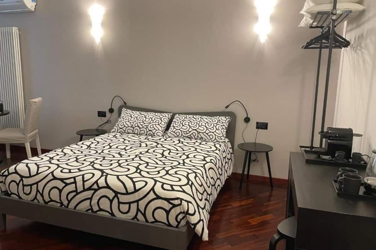 Un dormitori amb llit, taules de nit, una cadira, escriptori i una làmpada.