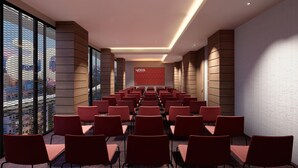 A conference room with rows of chairs, a large screen, and a city view through large windows.
