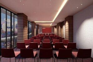 A conference room with rows of chairs, a large screen, and a city view through large windows.