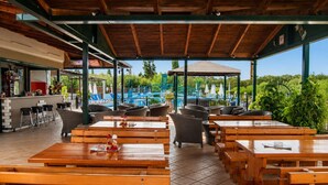 An outdoor café with wooden tables and chairs, a bar area, and a view of a pool and greenery. - Nikos Villas - Garden & Pool View Gem in Kavos (Kavos)