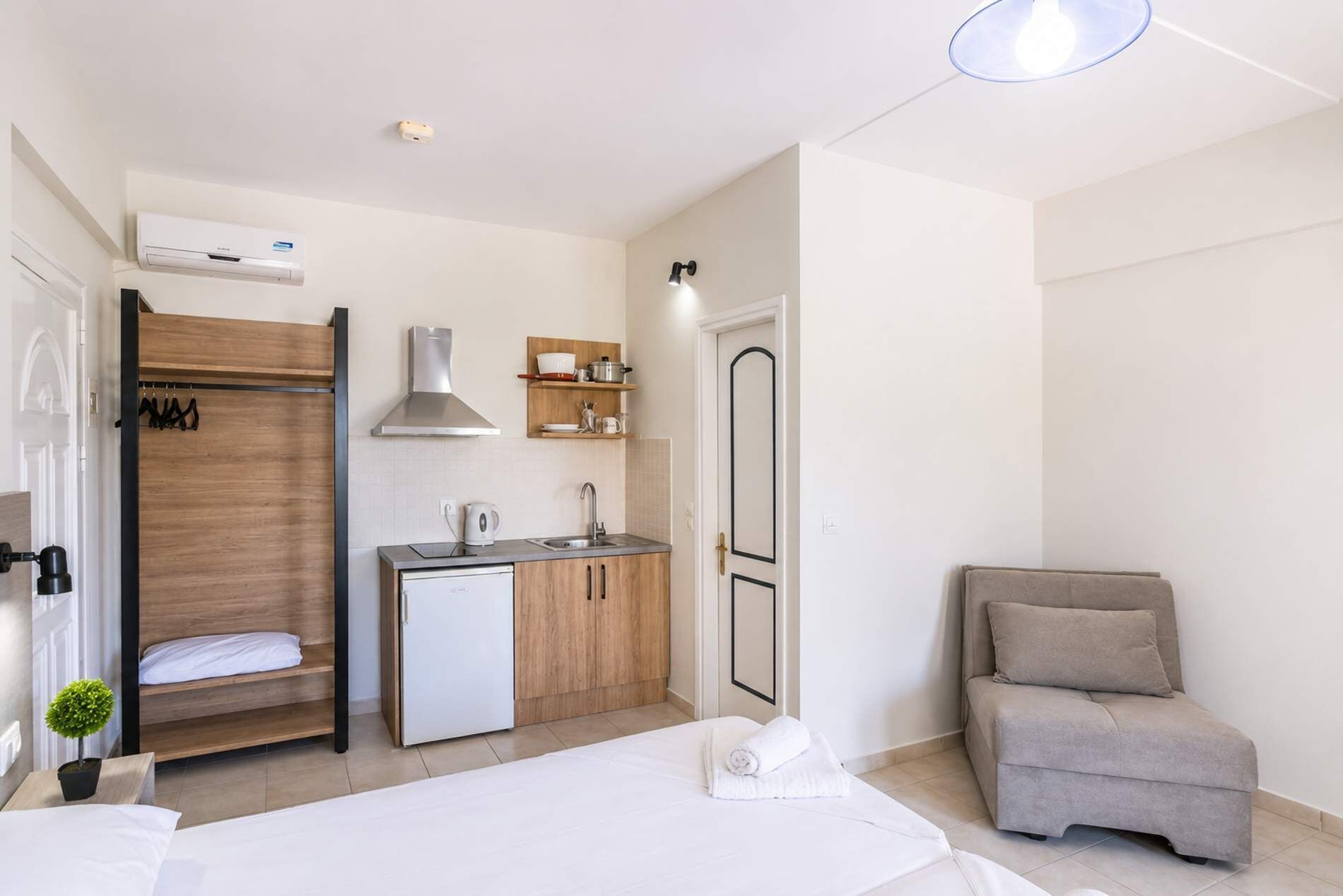 Une chambre d’hôtel compacte comprenant un lit, une petite kitchenette, un coin salon et une douche.