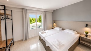 A hotel room with two beds, a wardrobe, a desk, and a view of greenery outside.