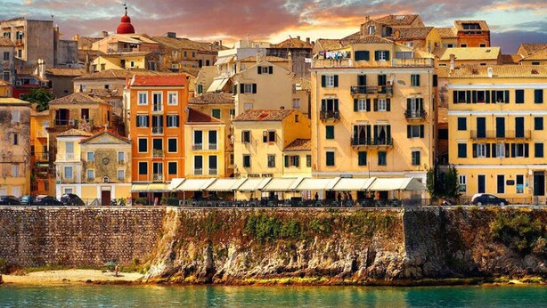 A coastal cityscape with historic buildings, a prominent red dome, and a stone wall overlooking the sea.