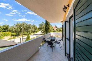 A balcony with a table and chairs, a door, and a view of trees and buildings.