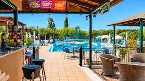 Et poolområde med liggestole, en bar og et overdækket siddeområde med udsigt til poolen.
