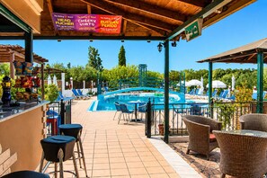 A pool area with lounge chairs, a bar, and a covered seating area with a view of the pool.