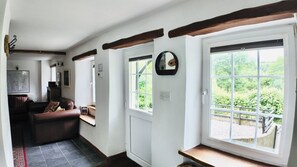 Ein Zimmer mit Kamin, einer Couch, einem Fenster mit Blick ins Grüne und einer Tür.