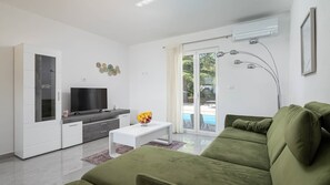 Ein modernes Wohnzimmer mit Flachbildfernseher, einer Couch, einem Esstisch und Blick auf einen Pool durch Glastüren.