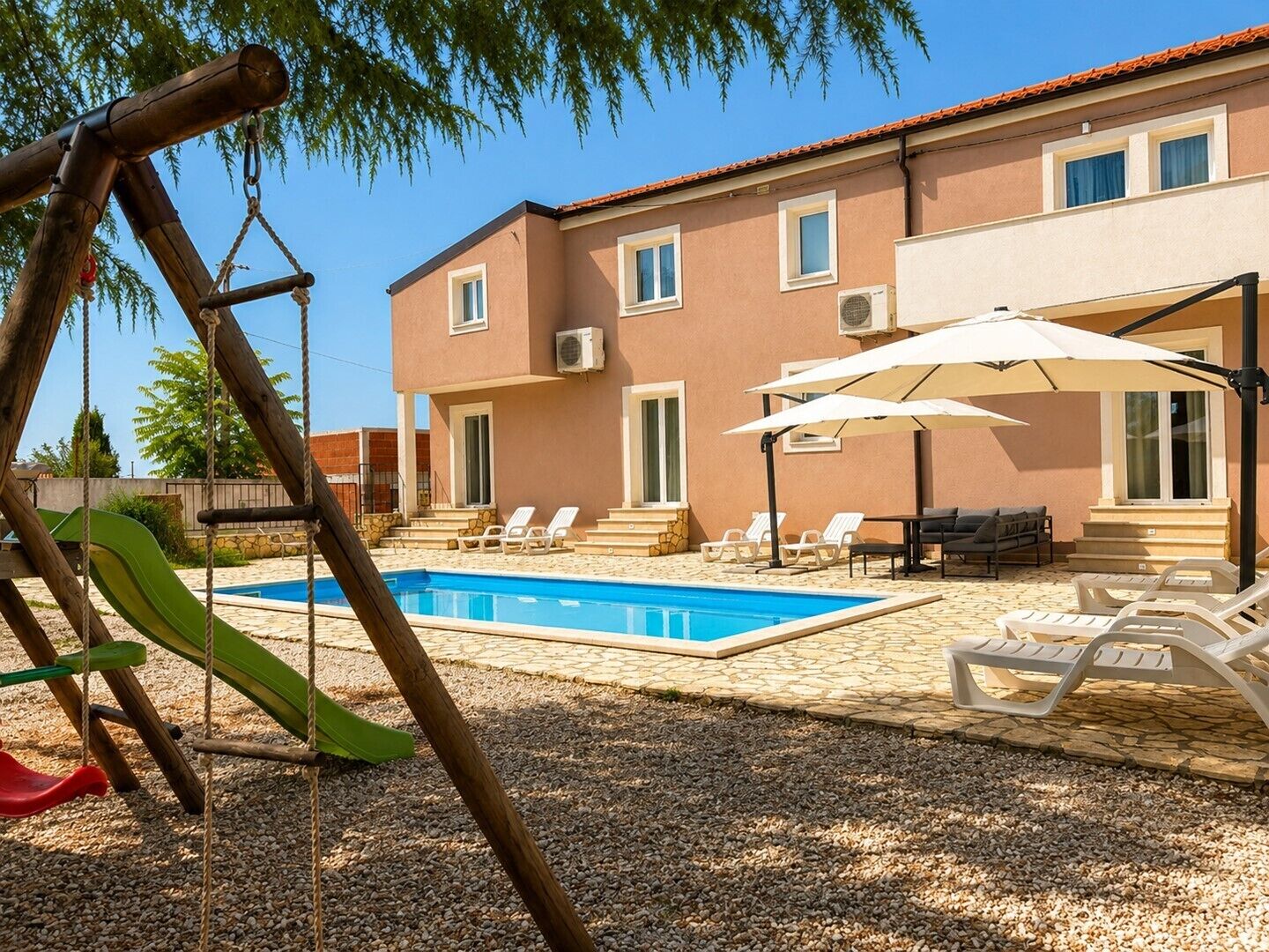 Area piscina con altalena, poltrone relax e un edificio con tetto in tegole.