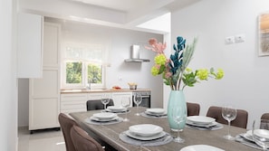 Ein moderner Essbereich mit einem Holztisch, gedeckt für sechs Personen, weißen Tellern und einer Vase mit Blumen.