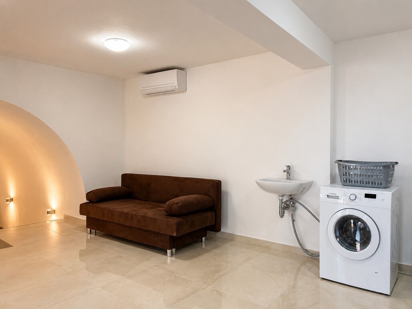 Un baño moderno con lavadora integrada, un lavamanos y un sofá marrón.