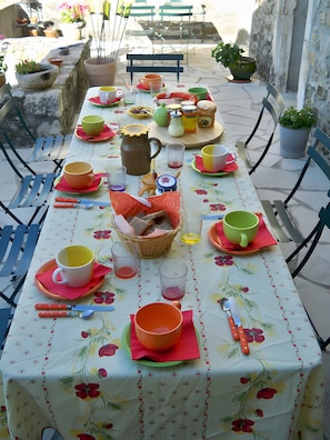 Una mesa preparada con diferentes platos, vasos y cubiertos, rodeada de sillas y macetas.