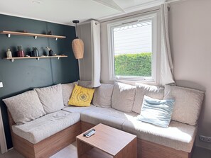 Ein modernes Wohnzimmer mit einem Ecksofa, einem kleinen Holztisch und einem Fenster mit Vorhängen.
