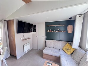 Ein modernes Wohnzimmer mit Ecksofa, einem Wand-Fernseher, einem Heizkörper und einer Wandablage mit Dekorationselementen.