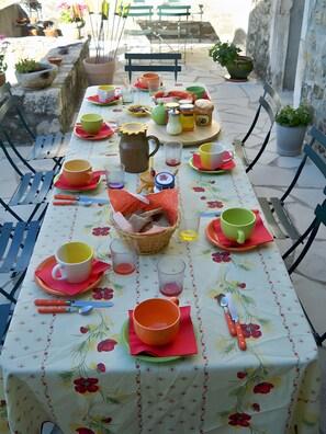 Une table dressée avec différents plats, des verres et des couverts, entourée de chaises et de plantes en pot.