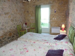 Une pièce comprenant un lit, une petite table, deux chaises, une lampe et une fenêtre avec un rideau.