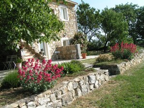 Uma casa de pedra com jardim, um muro de pedra e uma escadaria que leva à entrada.