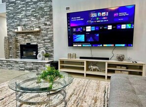 Ein modernes Wohnzimmer mit Flachbildfernseher, einer Wand aus Naturstein, einem Glastisch und einem gemütlichen Sofa.