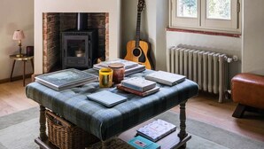 A cozy room with a fireplace, a guitar, a table with books, and a window with a view.